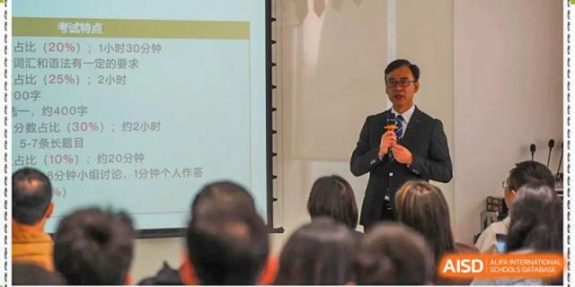 A man in a suit speaks at the front of a classroom while students listen attentively to his presentation at Yew Wah International Education School of Guangzhou