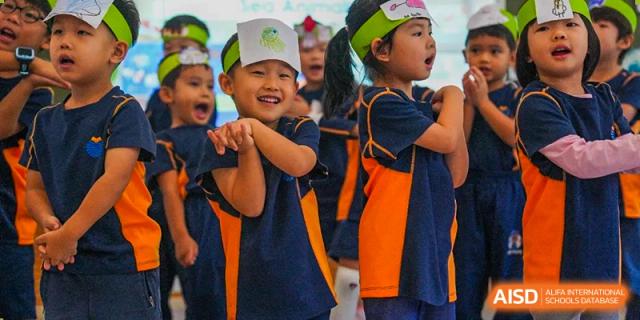 Two young boys in blue and orange uniforms smile and perform on stage during a school event or play at Yew Wah International Education School of Guangzhou