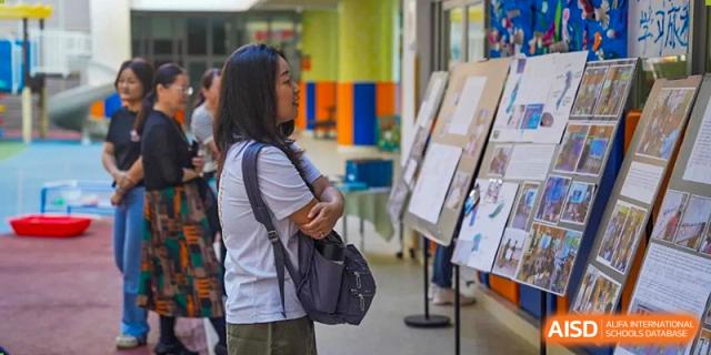 A woman with a purple backpack stands in a school hallway and looks at student work displayed on easels at Yew Wah International Education School of Guangzhou
