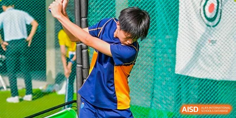 A male student in a blue and orange athletic uniform swings a bat during a game at Yew Wah International Education School of Guangzhou