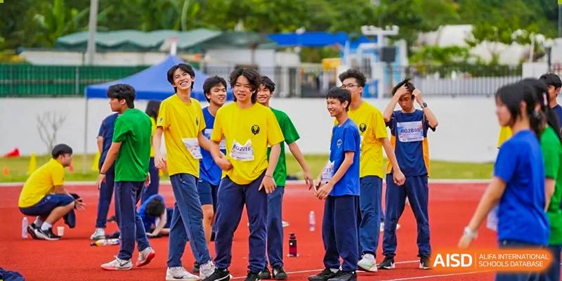 A group of students in yellow and blue sports uniforms walk together on a red running track at Yew Wah International Education School of Guangzhou