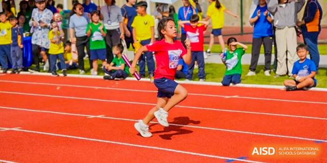 A young girl in a red shirt runs competitively on an outdoor track during a school sports day at Yew Wah International Education School of Guangzhou