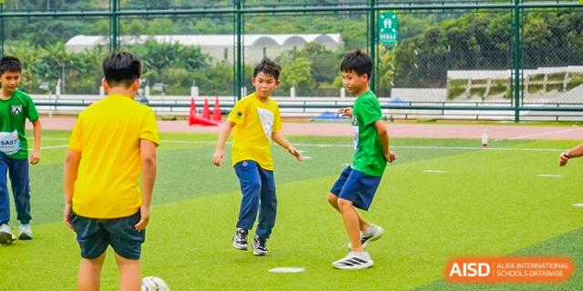 Two young boys in yellow and green shirts compete in a running drill on a grassy field at Yew Wah International Education School of Guangzhou
