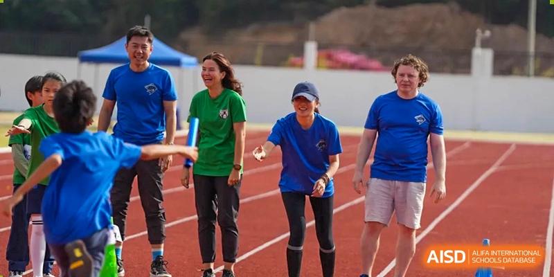 Two women in green and blue shirts smile while participating in an outdoor relay race at Yew Wah International Education School of Guangzhou