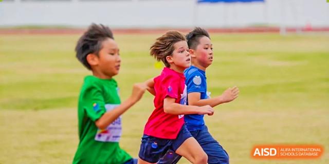 A young boy in a red shirt runs alongside other students during an outdoor track competition at Yew Wah International Education School of Guangzhou