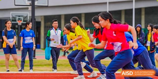 Young female students in yellow and red athletic wear prepare for a race on an outdoor track at Yew Wah International Education School of Guangzhou