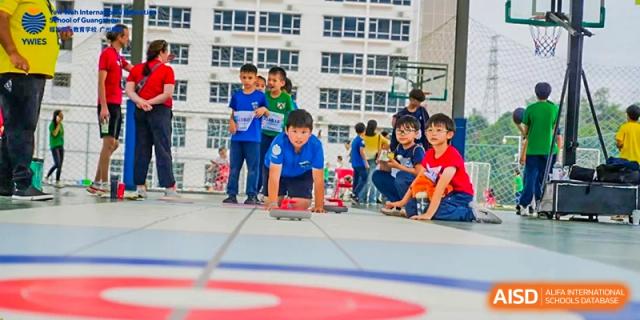 Several students sit and crouch on an indoor court prepared for a sports day activity at Yew Wah International Education School of Guangzhou