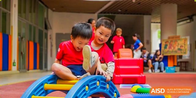 Two young boys in red shirts laugh while playing together on a blue playground structure at Yew Wah International Education School of Guangzhou