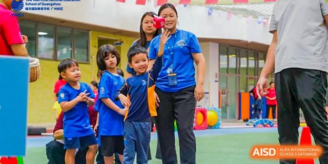 A teacher in a blue polo shirt stands with young students during an outdoor physical education class at Yew Wah International Education School of Guangzhou