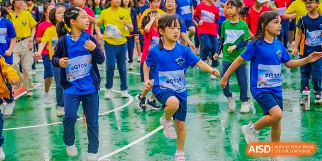 A young girl in a blue athletic shirt runs toward the camera during an outdoor sports activity at Yew Wah International Education School of Guangzhou