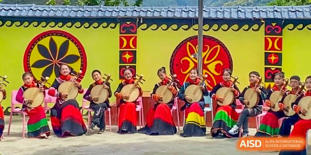 Three young students in traditional red and yellow attire play round stringed instruments outdoors at Yew Wah International Education School of Guangzhou