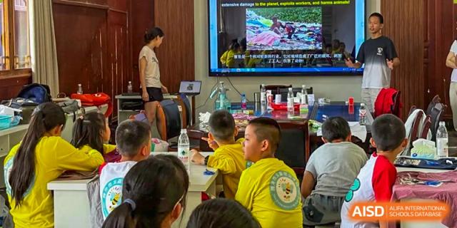 Students in yellow uniforms sit attentively in a bright classroom, watching an educational video presentation on a large screen at Beanstalk International Bilingual School Shunyi Campus.