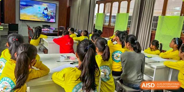A classroom full of students in matching yellow uniforms listens to a lecture, with educational posters displayed on the wall behind them at Beanstalk International Bilingual School Shunyi Campus.