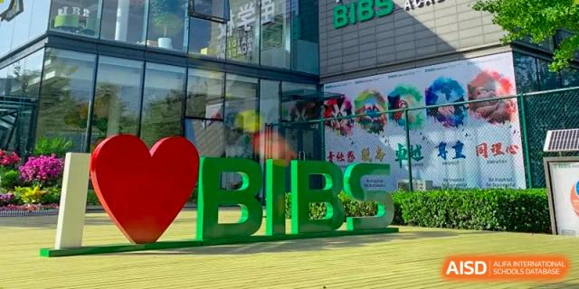 A large green outdoor sign reading "BIBS" stands next to a red heart sculpture in front of a modern glass school building at Beanstalk International Bilingual School Shunyi Campus.