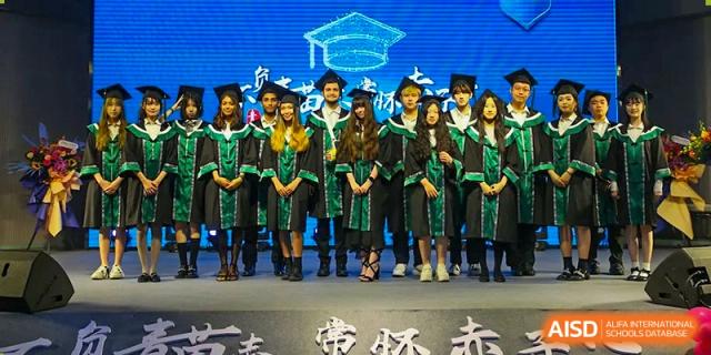 A row of graduating students in green and black academic gowns stand together on a stage during a formal commencement ceremony at Beanstalk International Bilingual School Shunyi Campus.