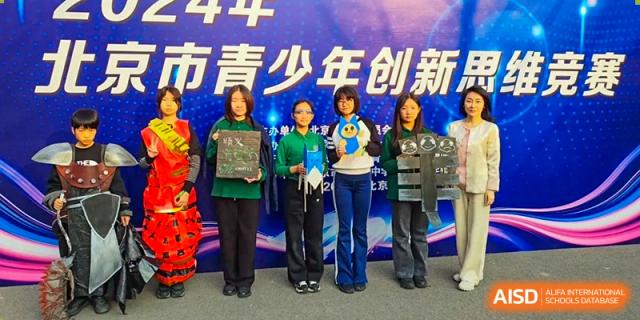 A group of female students and staff pose together while holding various awards and creative plaques following a successful competition at Beanstalk International Bilingual School Shunyi Campus.