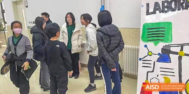 Students in casual winter clothing stand in a hallway, engaging in a relaxed conversation near educational displays between classes at Beanstalk International Bilingual School Shunyi Campus.