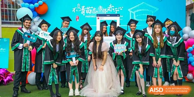 A group of joyful graduates in academic regalia pose together for a commemorative photo on the school lawn during graduation day at Beanstalk International Bilingual School Shunyi Campus.