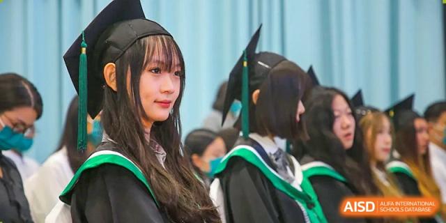 A close-up portrait of a female graduate wearing a black cap and a green-trimmed academic gown during the formal graduation processional at Beanstalk International Bilingual School Shunyi Campus.