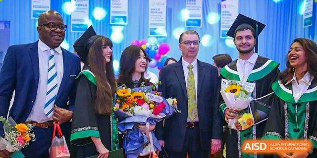Graduates in academic gowns and caps pose with a faculty member in a suit, holding bouquets and celebrating their achievement at Beanstalk International Bilingual School Shunyi Campus.