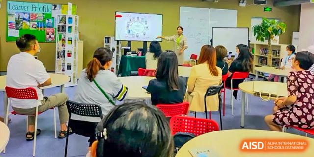 Educators participate in a professional development seminar, listening to a presentation displayed on a digital screen in a modern classroom at Beanstalk International Bilingual School Shunyi Campus.