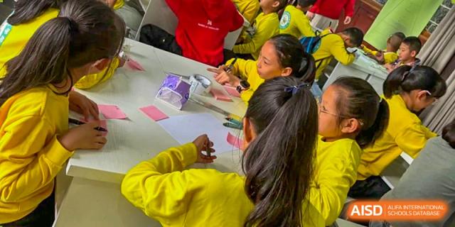 Students in yellow long-sleeved shirts work diligently on a collaborative project using sticky notes and creative materials on their desks at Beanstalk International Bilingual School Shunyi Campus.
