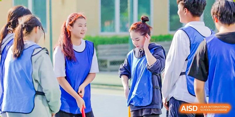 Two female students in blue sports vests stand on an outdoor court, holding floor hockey sticks and preparing for an active physical education match at Beanstalk International Bilingual School Shunyi Campus.