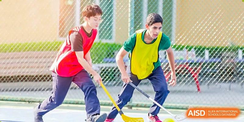 Two young male athletes compete in an intense floor hockey game on an outdoor sports court, demonstrating speed and focus during a physical education class at Beanstalk International Bilingual School Shunyi Campus.