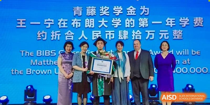 A student stands center stage in a green graduation gown, surrounded by faculty and distinguished guests during a formal academic awards ceremony at Beanstalk International Bilingual School Shunyi Campus.