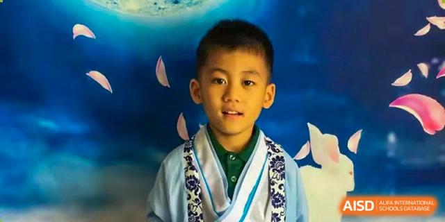 A young boy dressed in a formal light blue and white traditional robe poses confidently in front of a blue background featuring white rabbit motifs at Beanstalk International Bilingual School Shunyi Campus.