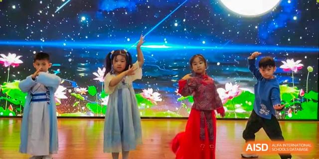 Two young girls perform a traditional dance on a stage decorated with lotus flowers and a starry night sky background during a school talent show at Beanstalk International Bilingual School Shunyi Campus.