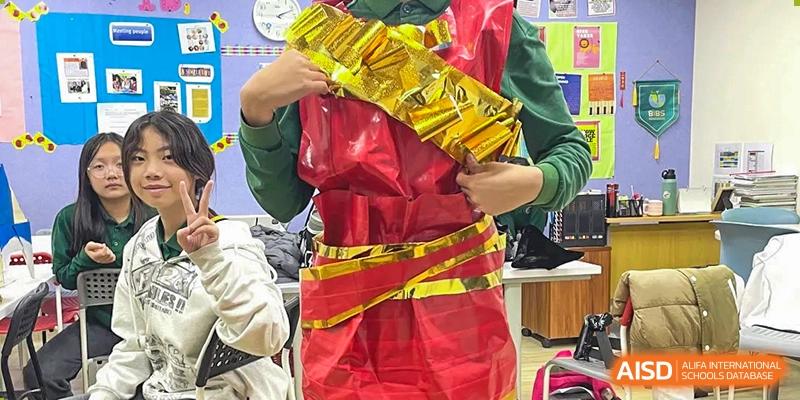 A student wears a creative and bulky costume made of shiny red and gold materials, participating in a fun recycled fashion project or drama activity at Beanstalk International Bilingual School Shunyi Campus.