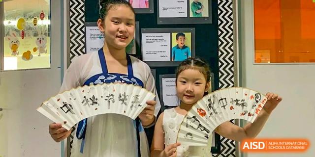 Two female students proudly display their hand-painted white folding fans, showcasing their artistic talents during a traditional Chinese art lesson at Beanstalk International Bilingual School Shunyi Campus.