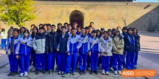 A large group of students in school uniforms poses for a commemorative group photo in front of a historic stone archway during a cultural campus excursion at Beijing LuHe International Academy.
