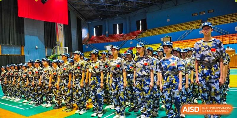 Rows of disciplined students in matching camouflage uniforms stand at attention in a large gymnasium during a formal assembly for the military training program at Beijing LuHe International Academy.