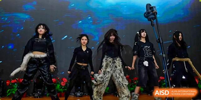 Three female students in edgy black outfits and stylish grey faux-fur leg warmers perform a modern dance routine on a stage with vibrant lighting at Beijing LuHe International Academy.