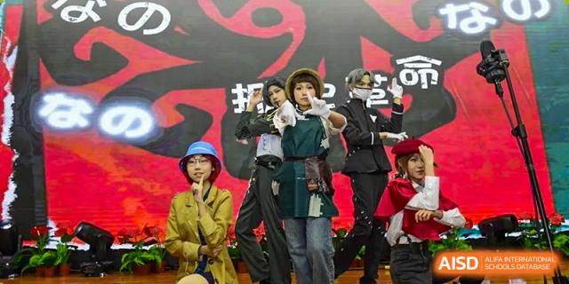 A group of students dressed in creative and eclectic costumes performs a theatrical skit or cosplay presentation on a stage with a red backdrop at Beijing LuHe International Academy.