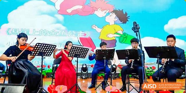 A small student ensemble featuring a flutist and a clarinetist performs musical scores in front of a bright animated screen during a concert at Beijing LuHe International Academy.