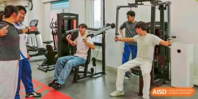 Three male students focus on their strength training routine by using various weight machines and resistance equipment in a modern campus gym facility at Beijing LuHe International Academy.
