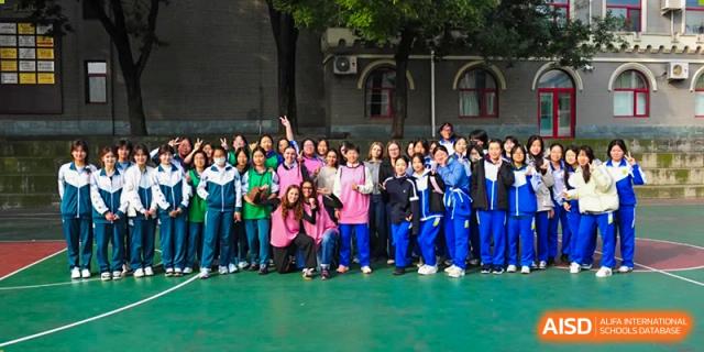 A large and diverse group of students in colorful sports jerseys and school uniforms poses together for a friendly team photograph on an outdoor green court at Beijing LuHe International Academy.