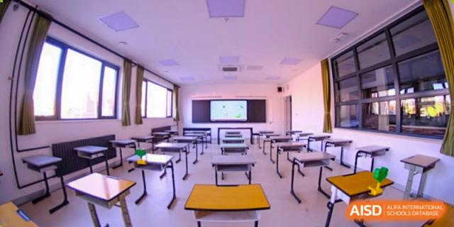 A bright and spacious classroom is shown with individual desks and chairs neatly organized in rows, featuring a digital whiteboard for interactive learning at Beijing Tongzhou Shuren Private School.