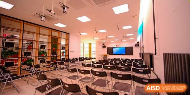 An empty modern lecture hall or multipurpose room is neatly arranged with rows of black chairs facing a large digital screen and presentation area at Beijing Tongzhou Shuren Private School.