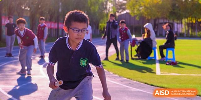 A young student in a navy blue polo shirt focuses intently while participating in an outdoor recreational activity on the school's paved grounds at Beijing Tongzhou Shuren Private School.