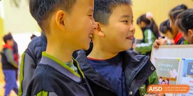 A close-up shot shows two young male students in their school uniforms sharing a smile and a conversation during a break between classes at Beijing Tongzhou Shuren Private School.