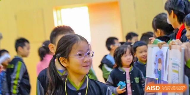 A young girl with glasses looks on with interest during a group classroom activity focused on interactive learning and peer discussion at Beijing Tongzhou Shuren Private School.
