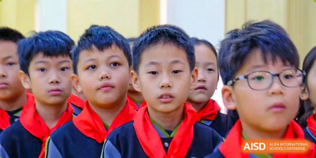 Three young students in formal school uniforms and red scarves look toward the camera with serious and attentive expressions during a lesson at Beijing Tongzhou Shuren Private School.