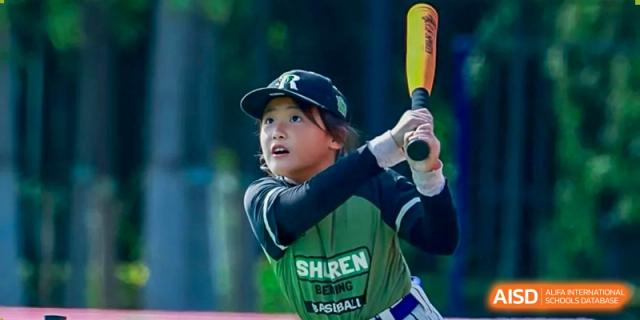 A young baseball player in a green and blue uniform keeps a sharp eye on the ball while holding a yellow bat, ready for the next pitch during a game at Beijing Tongzhou Shuren Private School.