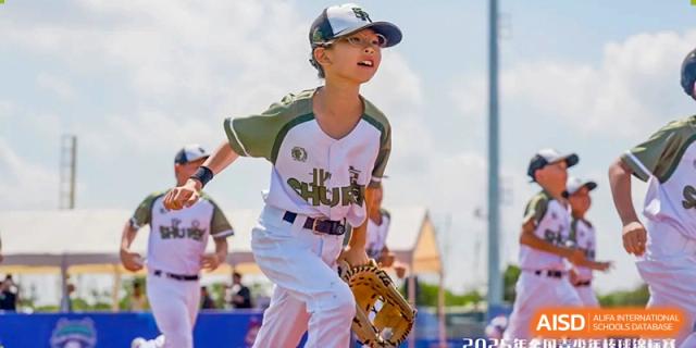 A focused baseball player in a white and green uniform runs across the diamond during an outdoor game, showcasing athletic spirit and teamwork at Beijing Tongzhou Shuren Private School.