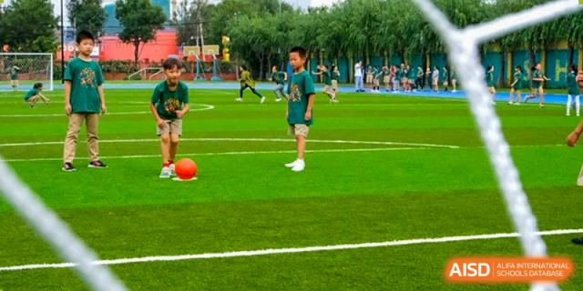 Young students participate in a soccer drill on a green field, practicing their footwork and coordination during a sunny outdoor sports class at Beijing Tongzhou Shuren Private School.