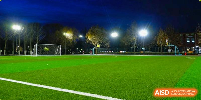 The school's artificial turf sports field is illuminated by bright stadium lights under a dark evening sky, ready for night-time athletic practice at Beijing Tongzhou Shuren Private School.